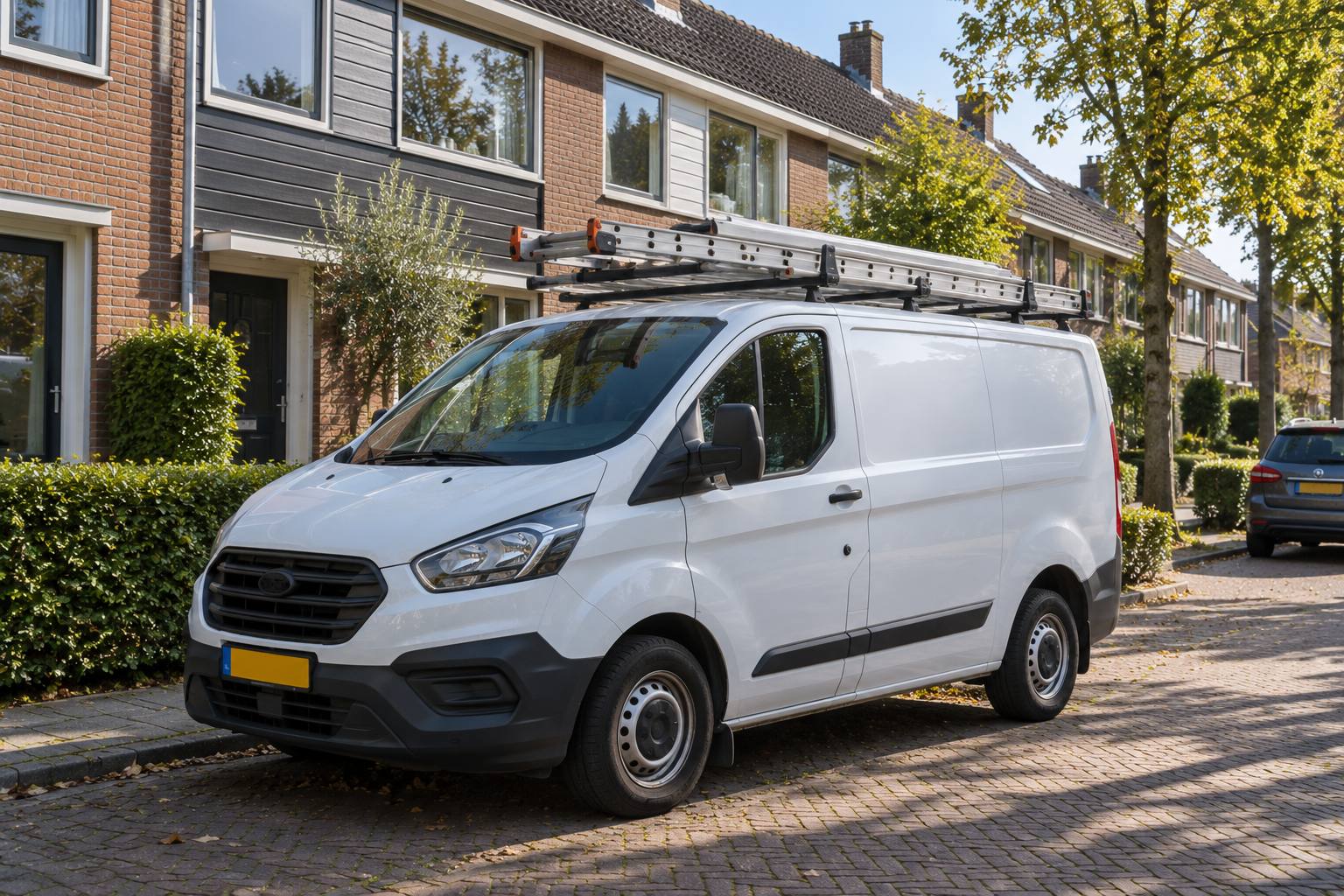 Witte bedrijfsbus met ladders op het dak in een straat met rijwoningen