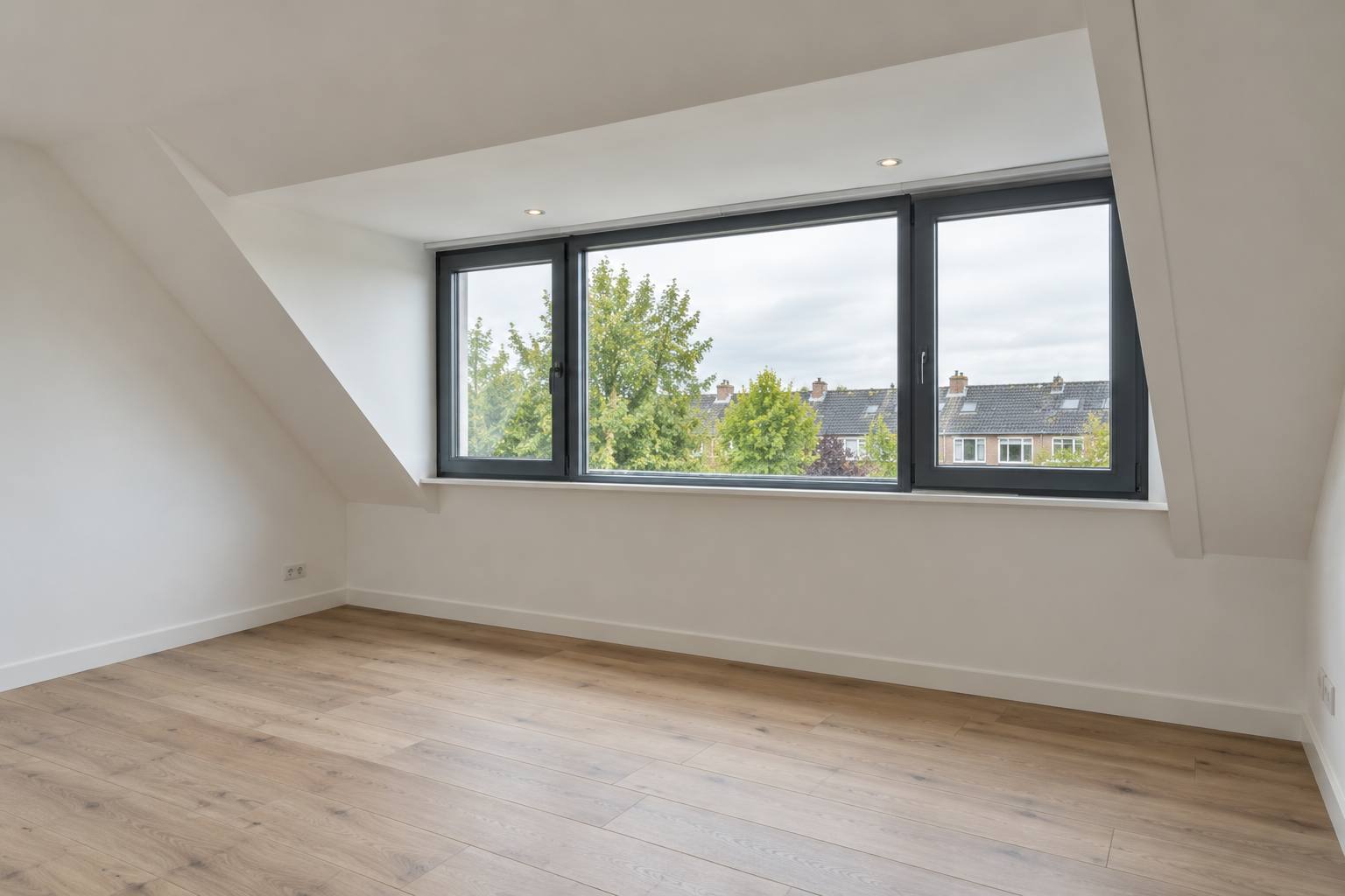 Verbouwde zolder met houten vloer en een dakkapel met drie ramen